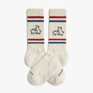 The Keith Haring Two Dogs - Athletic socks feature a cream base with red and blue top stripes, black outlined dogs facing each other, and black text near the toes—ideal for unique finds at a Tallinn shopping or gift shop. Gate21.ee