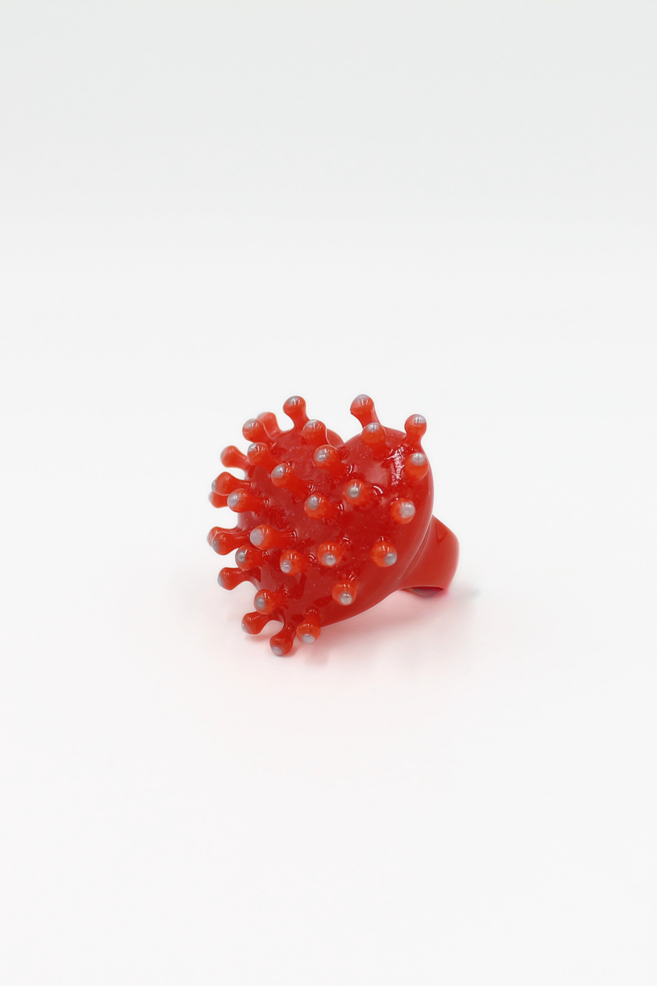 A “Virus - Ring” in bold red, designed by CACKO with a round, spiky form reminiscent of a virus or sea urchin, is displayed in the centre against a plain white background. Gate21.ee