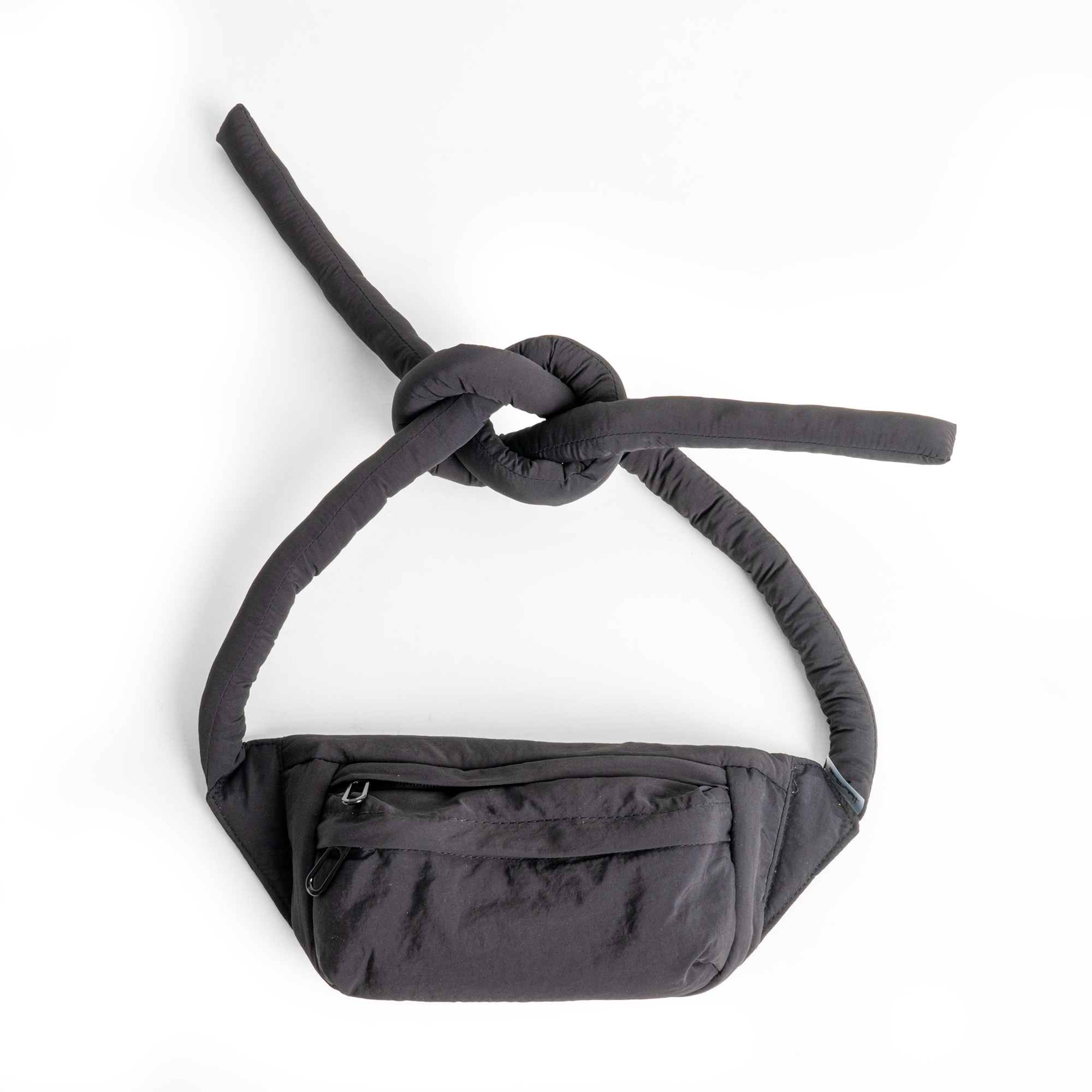 The Knotflex Pack - Black is a stylish waist bag featuring two long, padded straps tied in a knot and a front zipped pocket. Displayed on a white background, it’s perfect for creative projects or gift shop selections. Gate21.ee