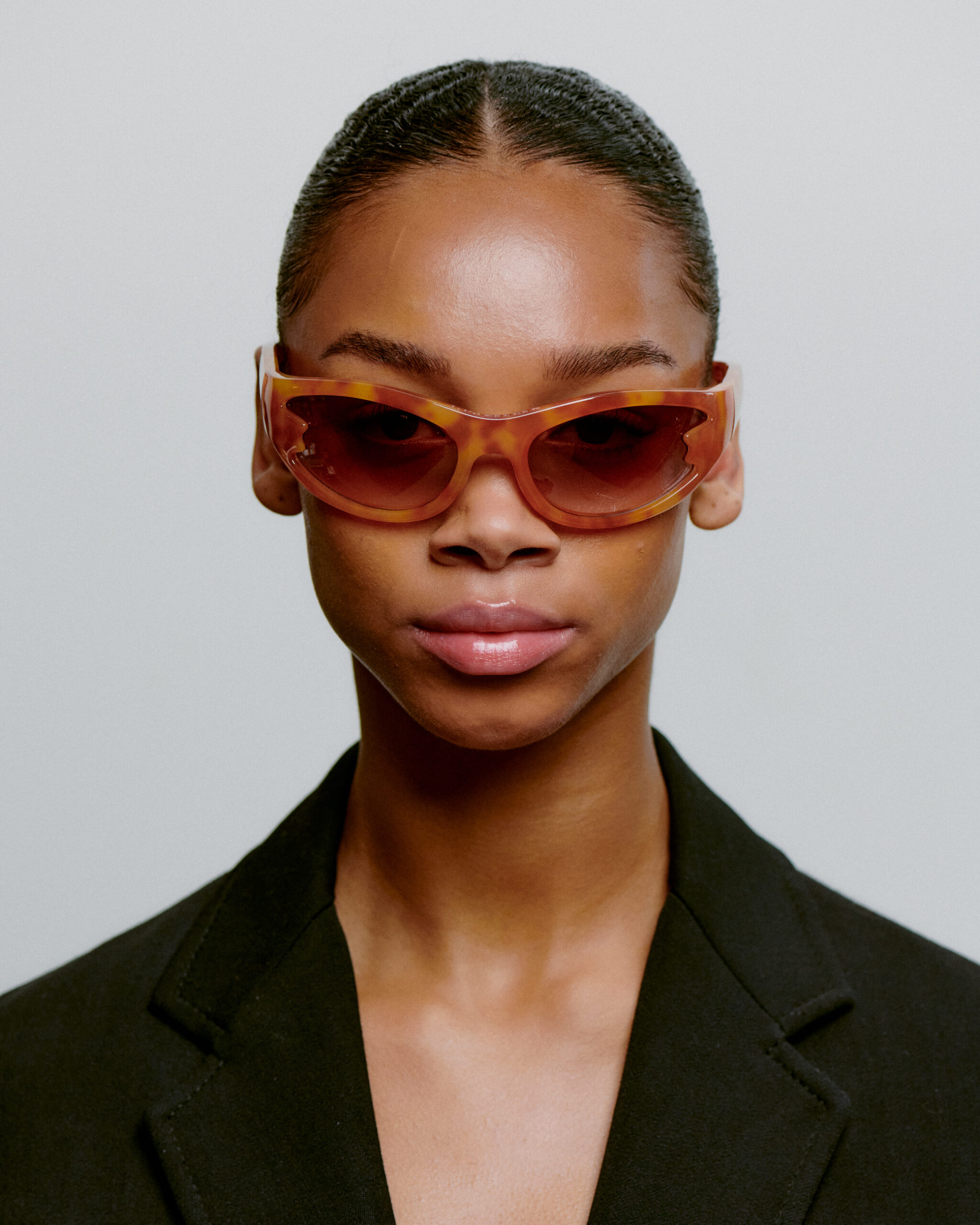 Wearing BLAST - Burnt Amber brown cat-eye sunglasses and a black blazer, a person with slicked-back hair looks confidently at the camera against a plain light background—capturing effortless, curated Tallinn style. Gate21.ee
