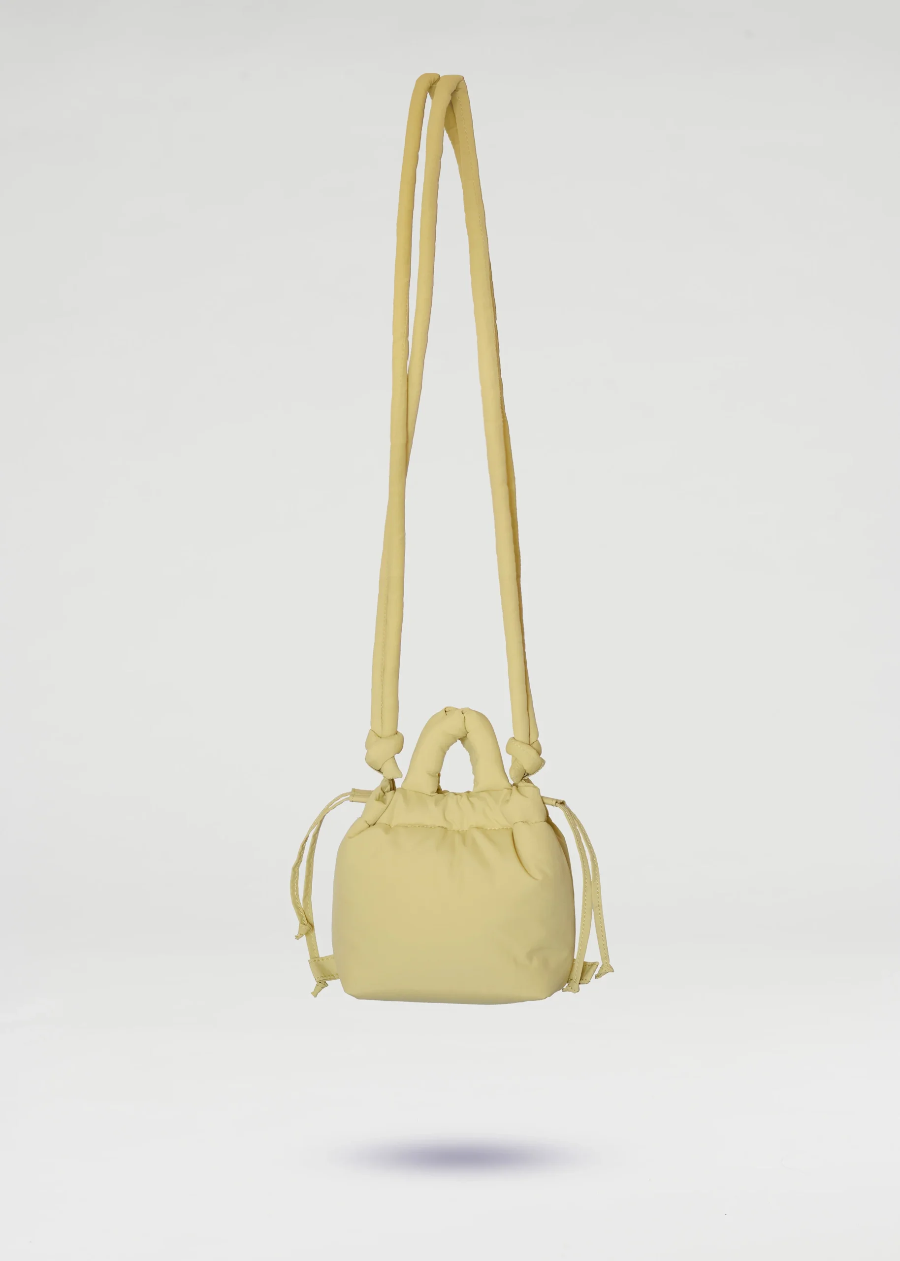 The Micro Ona Soft Bag - Lime is a small, pale yellow handbag featuring a long shoulder strap, short handles, and side drawstring details—perfect for curated concept shop collections or anyone after a distinctive accessory. Gate21.ee