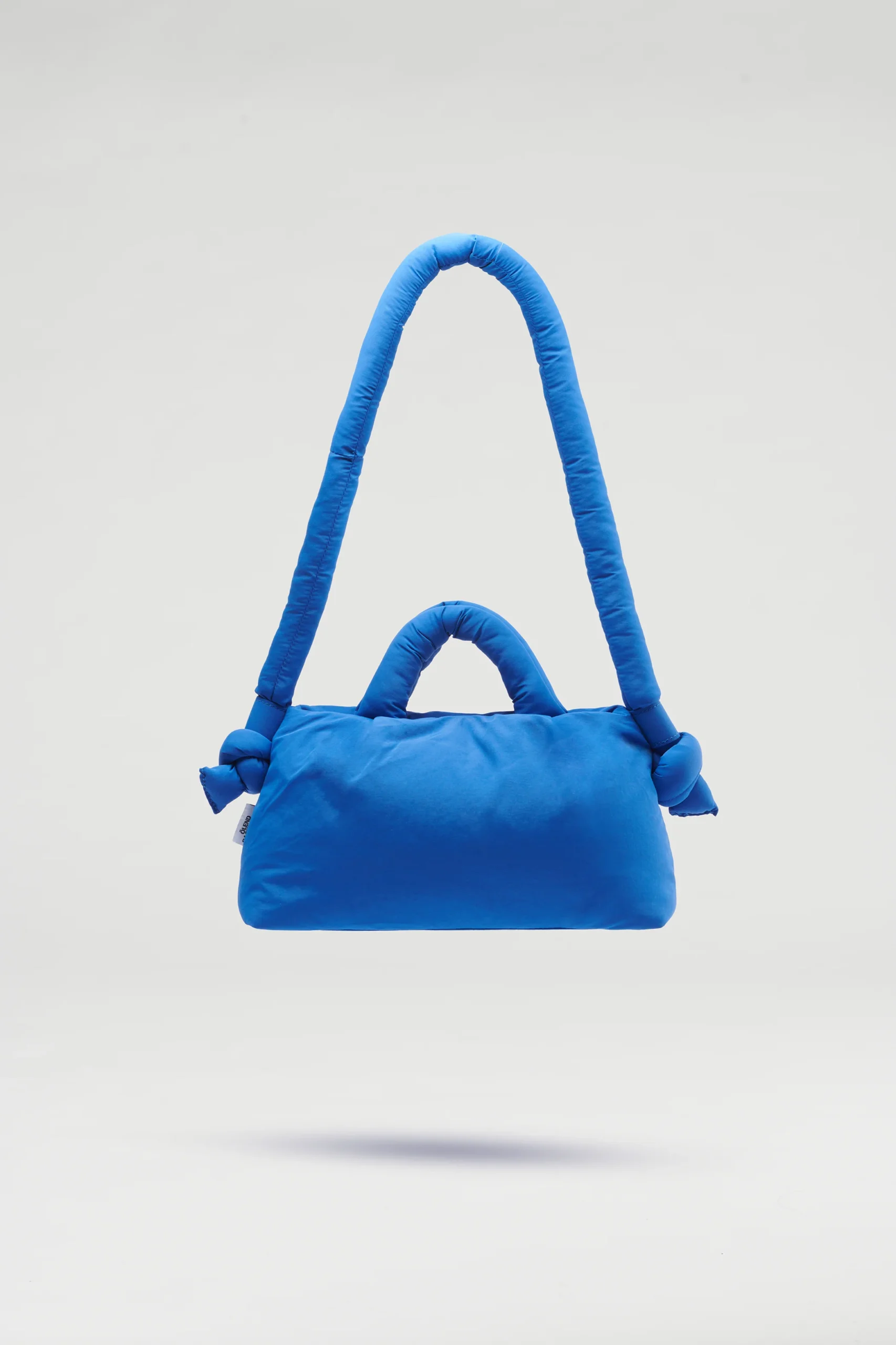 The Mini Ona Soft Bag - Cobalt Blue is a bright blue, rectangular padded handbag with a thick cushioned strap and knotted ends, showcased on a light grey background—a distinctive piece of Estonian design ideal for concept shops. Gate21.ee