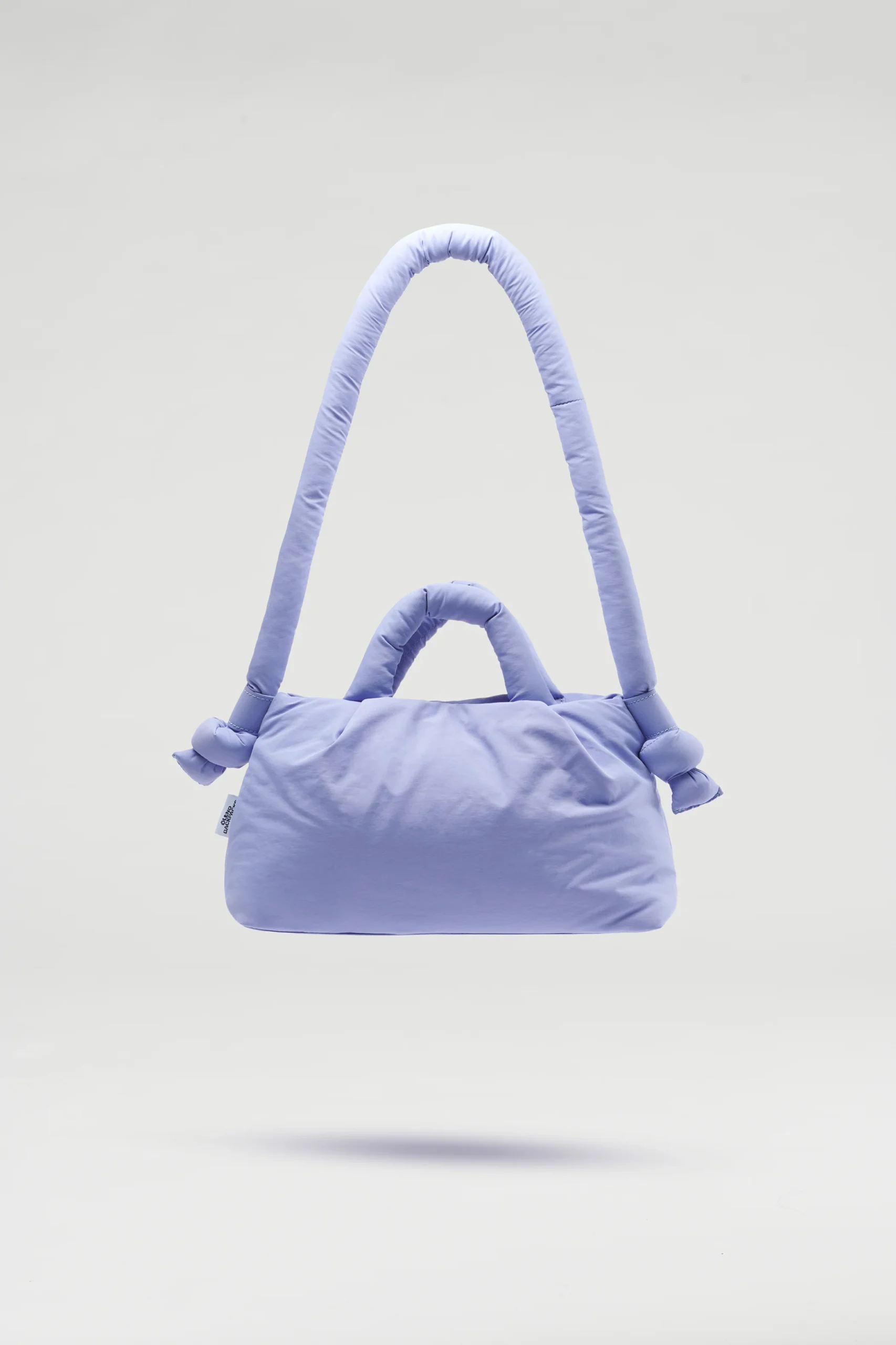 The Mini Ona Soft Bag - Lilac, a padded light purple handbag with a thick shoulder strap and two short handles, is displayed against a plain grey background—ideal for Tallinn shopping or as a charming gift shop find. Gate21.ee