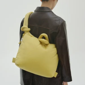 Seen from behind, a person with dark hair tied back wears a dark brown leather jacket and carries the Ona Soft Bag - Lime, a large padded Estonian-designed bag with knotted handles, over their shoulder against a plain background. Gate21.ee