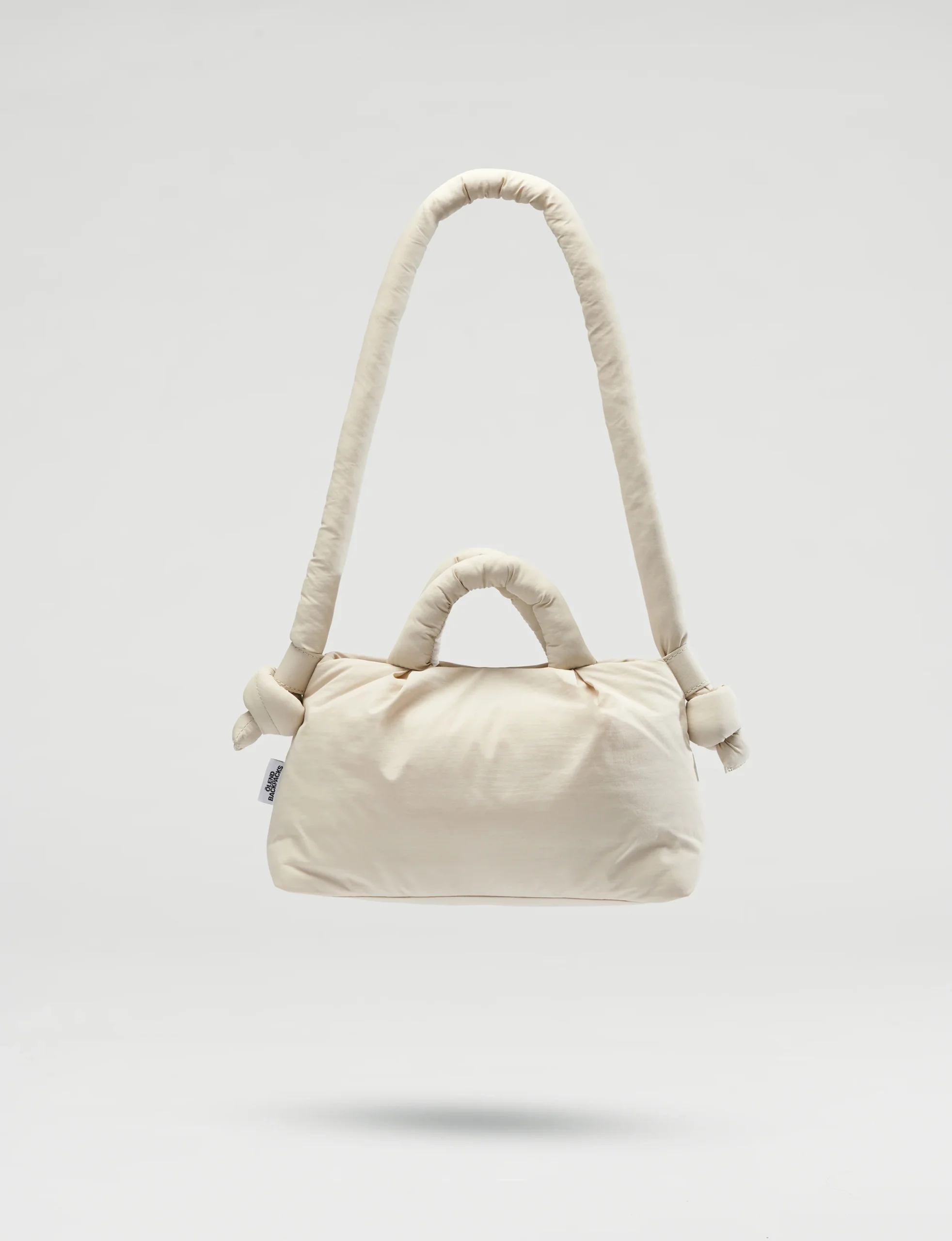 The Mini Ona Soft Bag - Sand is a cream-coloured, padded handbag with a long, rounded shoulder strap, two short handles with knot details, and Estonian design elegance—displayed against a plain light background. Gate21.ee