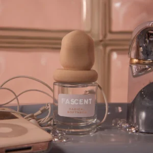 A 30ml bottle of Radical Softness &ndash; FASCENT with a rounded beige cap sits beside earphones, a mobile phone, and a metallic object, highlighting Estonian design against glass tiles. Gate21.ee