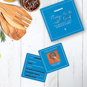 A tabletop shows a blue box labelled “Dad - Scratch Cards,” perfect for fun moments. Two cards are visible: one says “Cook a meal together,” while the other suggests cooking pasta and watching a film. Gate21.ee