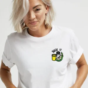 A person with short blonde hair wears the Suck it Tequila T-Shirt - White, featuring an embroidered cup, snake, and "Suck It" text on the upper left—a quirky gift or fun Tallinn shopping find. Gate21.ee