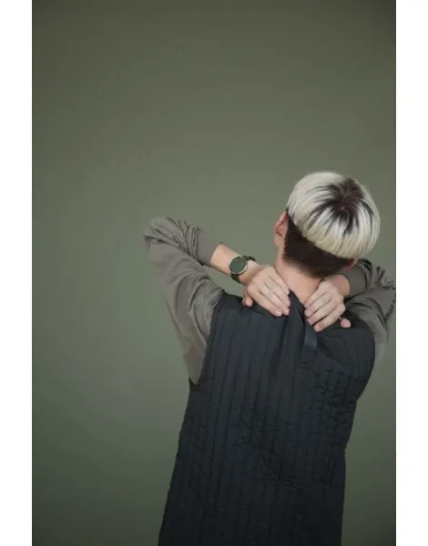 A person with short, two-toned hair is seen from behind, wearing a long-sleeved shirt and waistcoat, hands on their neck—a striking scene to showcase the Olive / Olive / 40mm in a concept store or gift shop focused on modern style. Gate21.ee