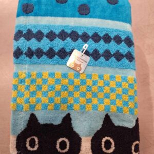 The Bath Towel - KÕIK - 120cm features blue, turquoise, and yellow geometric patterns with dots, diamonds, and chequerboards, plus a row of black cat faces at the bottom—a playful Estonian design with a tag on one corner. Perfect for gift shops. Gate21.ee
