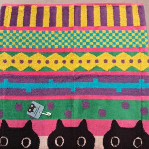 The Wash towel 36cm - KÕIK features bright horizontal stripes in yellow, green, teal, purple, and pink with black cartoon cat faces along the bottom—a fun Tallinn gift shop find for anyone seeking playful and unique souvenirs. Gate21.ee