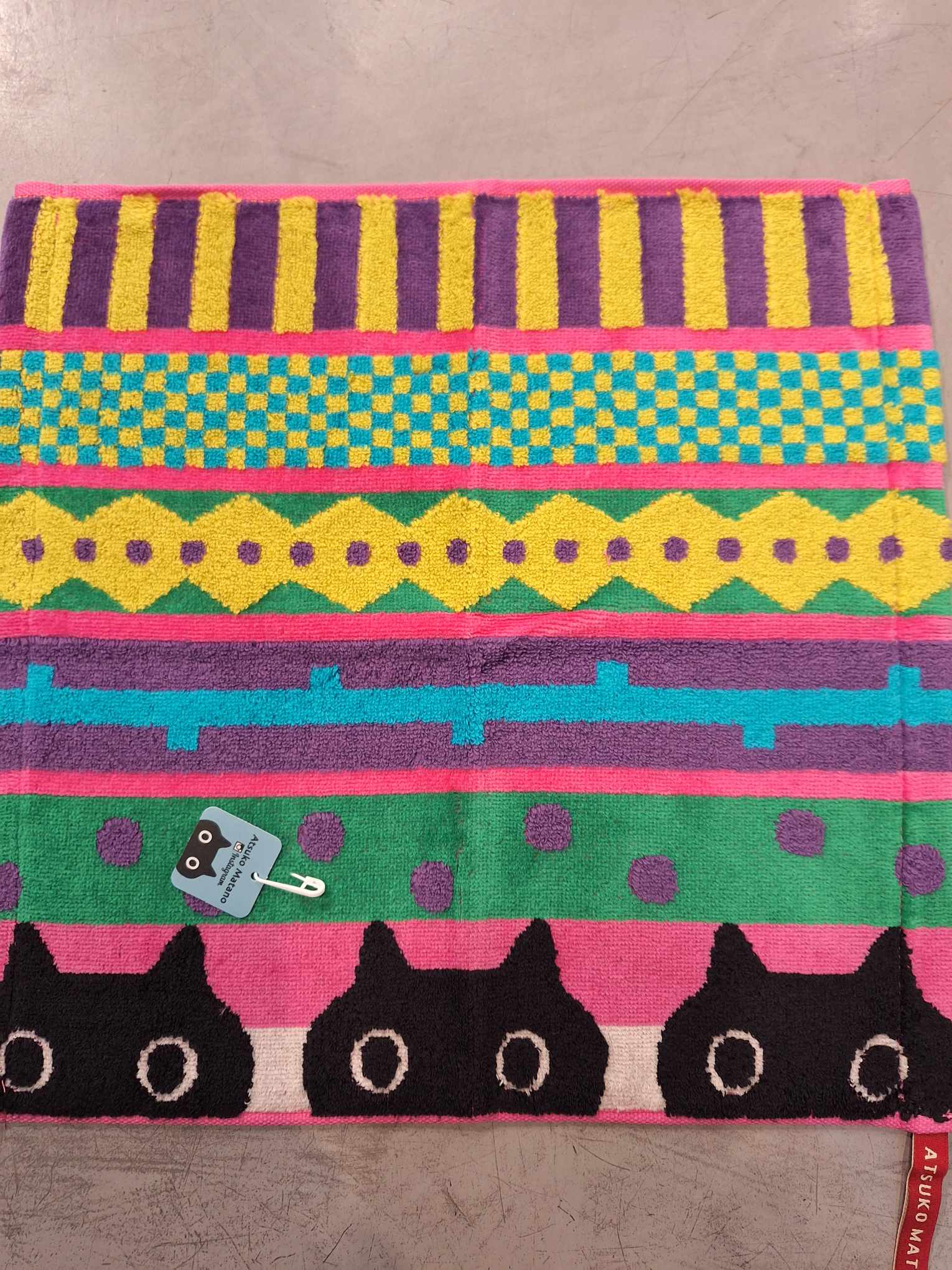 The Wash towel 36cm - KÕIK features bright horizontal stripes in yellow, green, teal, purple, and pink with black cartoon cat faces along the bottom—a fun Tallinn gift shop find for anyone seeking playful and unique souvenirs. Gate21.ee