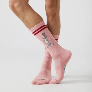 A person wearing Duffy & Bugs Bunny - Athletic socks, featuring pink colour, red stripes, and a cartoon rabbit design inspired by Estonian style, stands against a plain white background. Gate21.ee