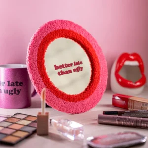 The "Better late than ugly!" mirror features a pink and red textured frame and playful phrase, making it a standout piece for concept shops seeking unique make-up-themed décor. Gate21.ee