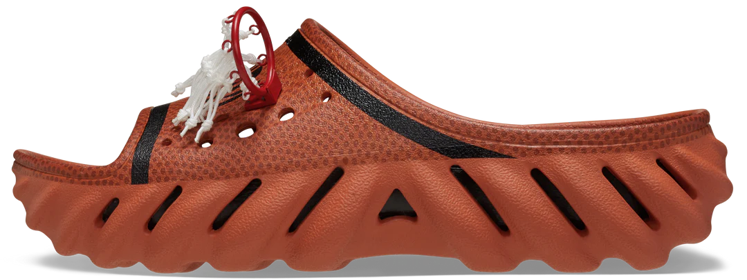 A side view of a Crocs™ NBA Echo Slide in Sienna showcases its textured, ventilated design, bold black accents, red loop detail, and sculpted sole—ideal for concept shops seeking standout footwear ideas. Gate21.ee