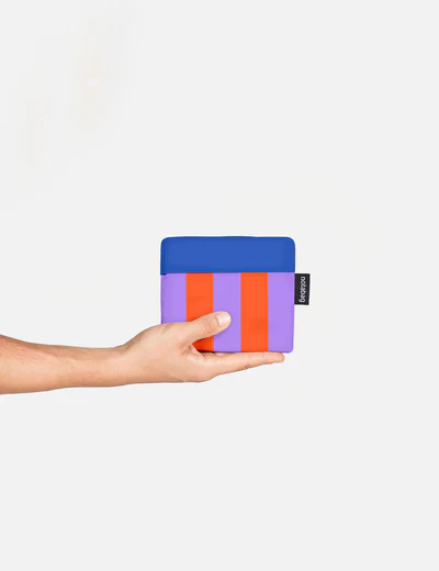 A hand holds the "Royal Stripes - Special Edition" pouch, featuring a blue top, purple body, and two red stripes with a black label on a plain white background—an eye-catching Tallinn gift shop find. Gate21.ee