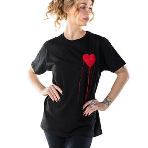 A woman with light brown curly hair wears the LUKS - 1 Süda T-shirt, a black shirt featuring a red dripping heart—a standout Estonian design. She poses confidently against a white background—ideal for unique Tallinn shopping finds. Gate21.ee