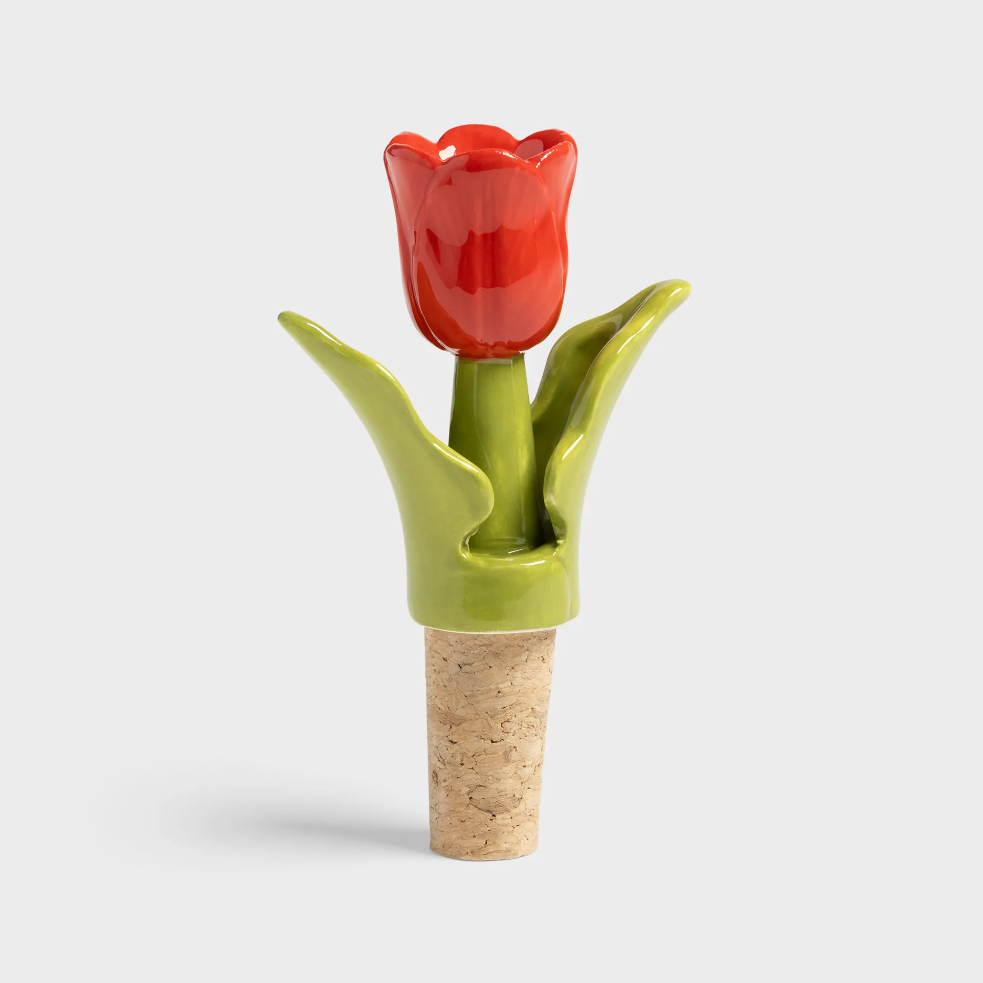 The Bottle Stopper Tulip - Red (7 x 3.5 x 12 cm) features a cork base and a ceramic top shaped and painted like a red tulip with green leaves—an ideal unique gift shop find against a simple, light background. Gate21.ee