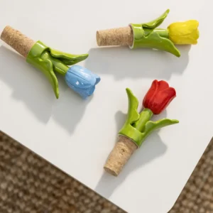 A Bottle Stopper Tulip in yellow (7 x 3.5 x 12 cm) with a ceramic tulip, green stem, and cork base lies on a white surface—an ideal addition to any concept shop or Tallinn shopping trip. Gate21.ee
