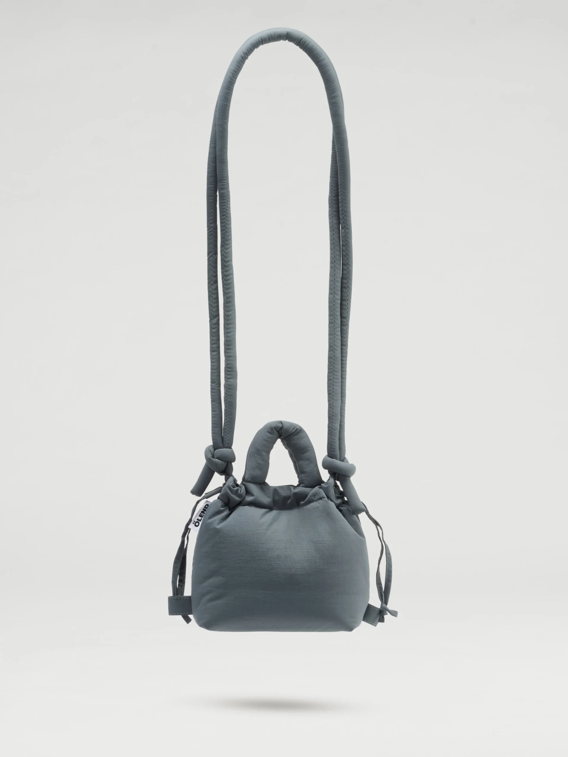 The Micro Ona Soft Bag - Coal is a compact, grey padded crossbody with a long strap, short handles, side drawstrings, and a minimalist look—perfect for concept shops—shown against a plain white background. Gate21.ee