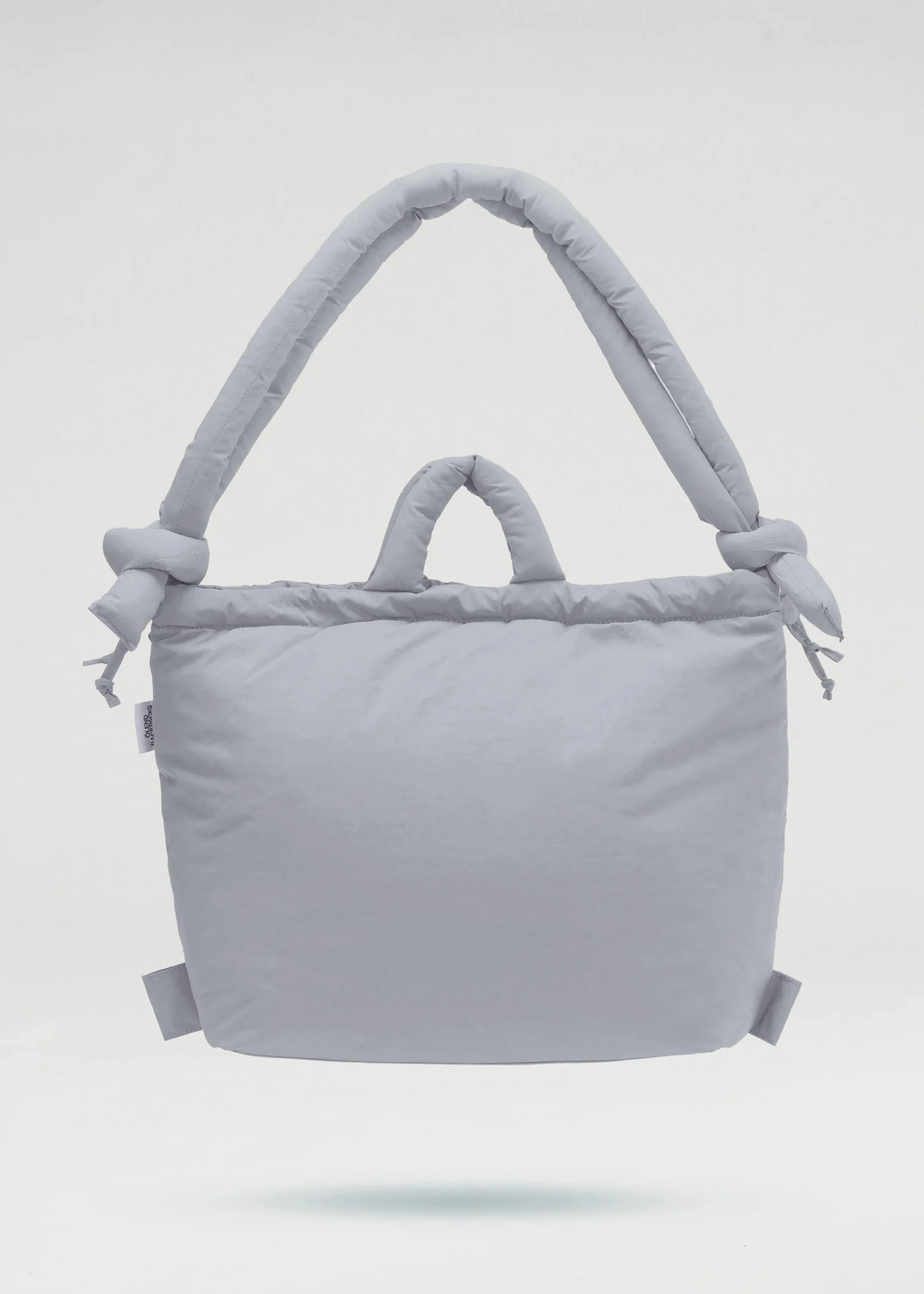 The Ona Soft Bag - Grey is a padded tote with two short handles and two long, knotted shoulder straps. Its plain, soft design is featured against a white background, curated for a modern concept shop. Gate21.ee