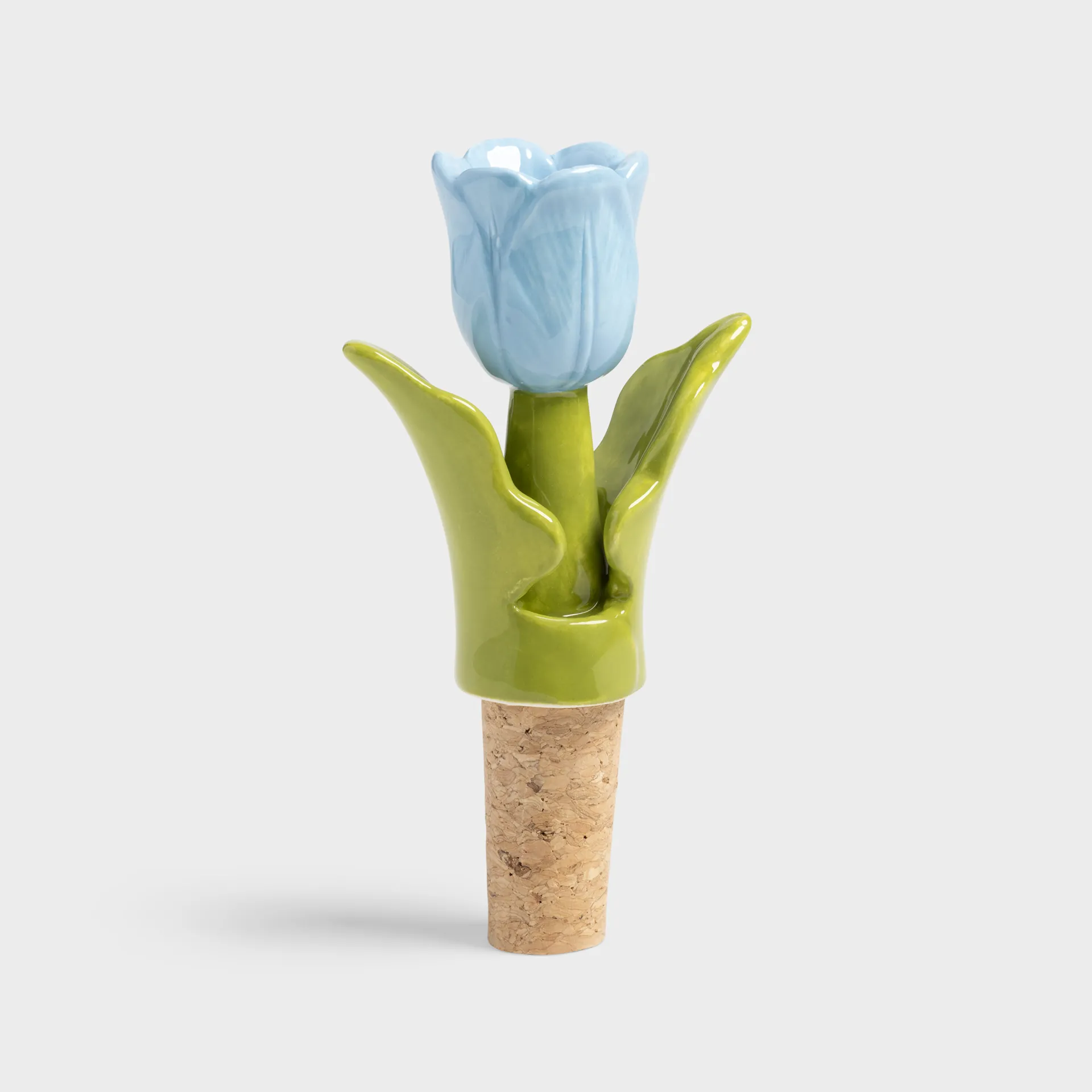 The Bottle Stopper Tulip - Blue (7 x 3.5 x 12 cm) features a cork base and a ceramic top shaped like a blue tulip with green leaves—a distinctive Estonian design, perfect for Tallinn shopping or as a unique gift. Displayed on a plain light grey background. Gate21.ee