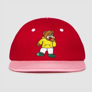 The Teddyarchy Cap is a red baseball cap with a pink peak, showcasing an embroidered cartoon bear in a yellow shirt, white trousers, and green shoes. Ideal for curated gift shops or playful Estonian design fans. Light grey background. Gate21.ee