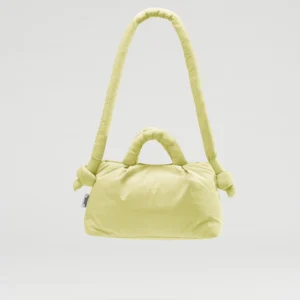 The Mini Ona Soft Bag - Lime is a light yellow padded handbag with short handles and a long, knotted shoulder strap, displayed against a plain light grey background—a chic, plush accessory for stylish shoppers. Gate21.ee