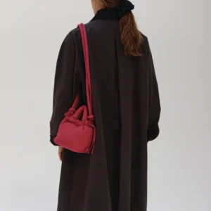 A person with long brown hair tied back, dressed in a dark coat, carries the Micro Ona Soft Bag in Cherry Red over their shoulder. They face away from the camera against a plain background, highlighting this standout gift shop find. Gate21.ee
