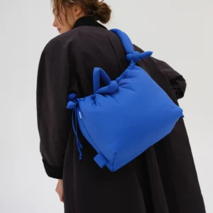 Seen from behind against a plain white background, a person in a loose black coat carries the Ona Soft Bag in cobalt blue, featuring padded construction, knotted handles, and drawstring details—an eye-catching Estonian design. Gate21.ee