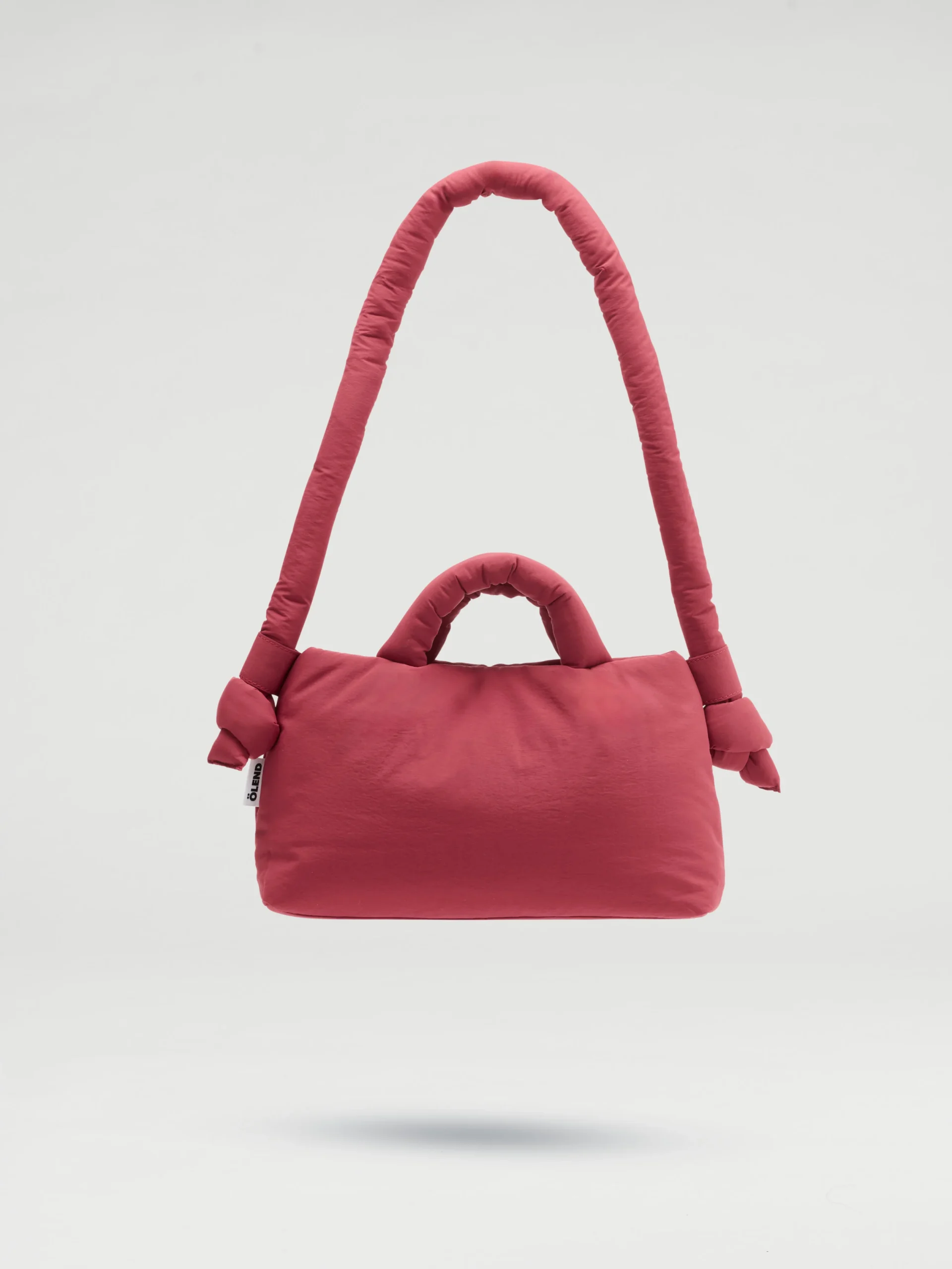The Mini Ona Soft Bag - Cherry Red, featuring padded handles and a cushioned shoulder strap, stands out against a white background—an on-trend accessory you’d find in a stylish Tallinn concept shop. Gate21.ee
