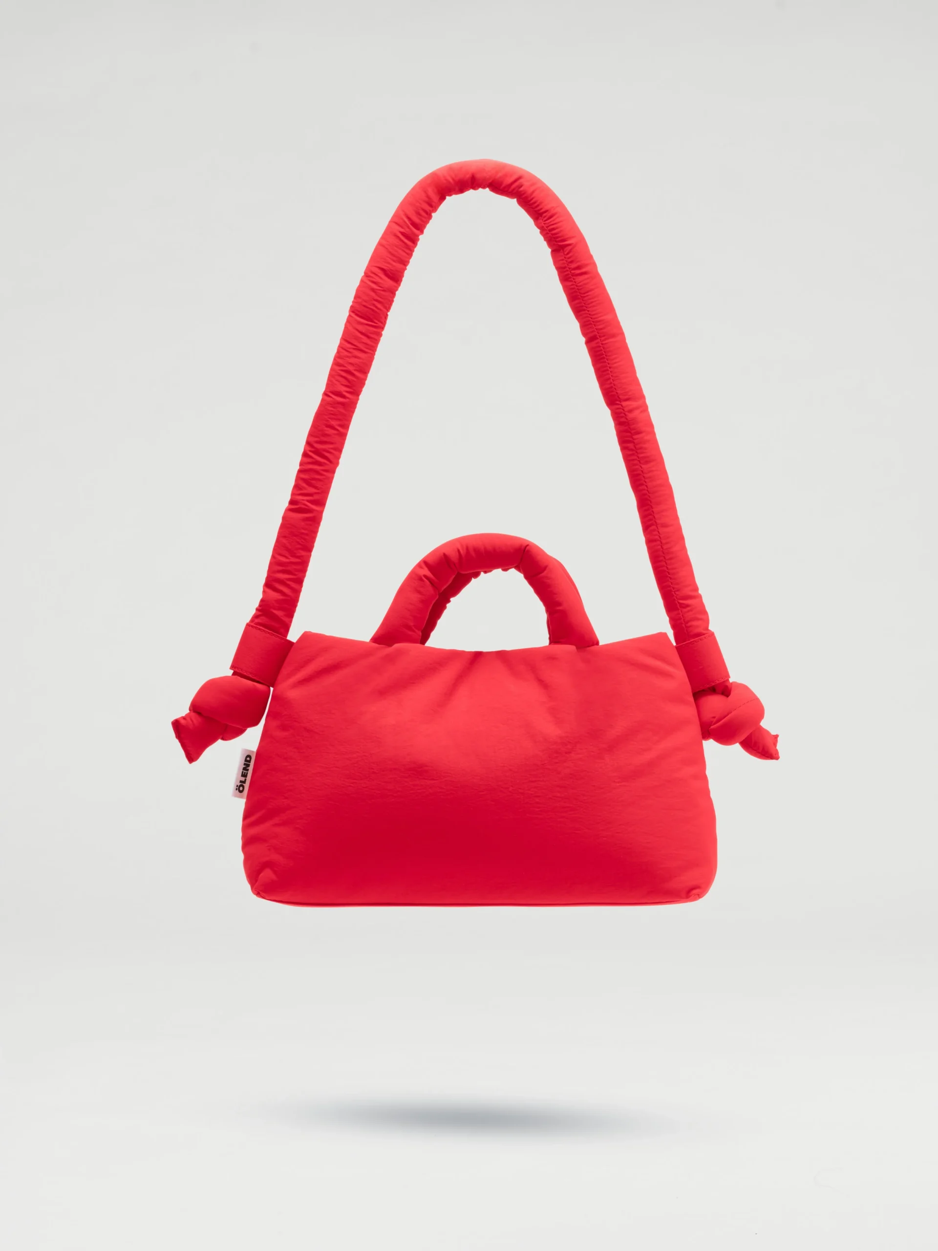 The Mini Ona Soft Bag - Red is a bright padded handbag with short handles and a long, knotted strap, highlighting unique Estonian design, displayed against a plain light background. Gate21.ee
