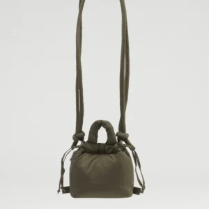 The Micro Ona Soft Bag in forest green, with long padded straps and knotted details, hangs against a plain light grey background. Showcasing Estonian design, this small bag has a soft, puffy look and features a drawstring fastening. Gate21.ee