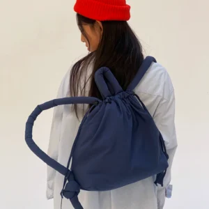 A person with long dark hair, in a red knitted beanie and white shirt, is seen from behind carrying the Ona Soft Bag - Navy—a stylish drawstring rucksack perfect for those seeking unique accessories. Gate21.ee