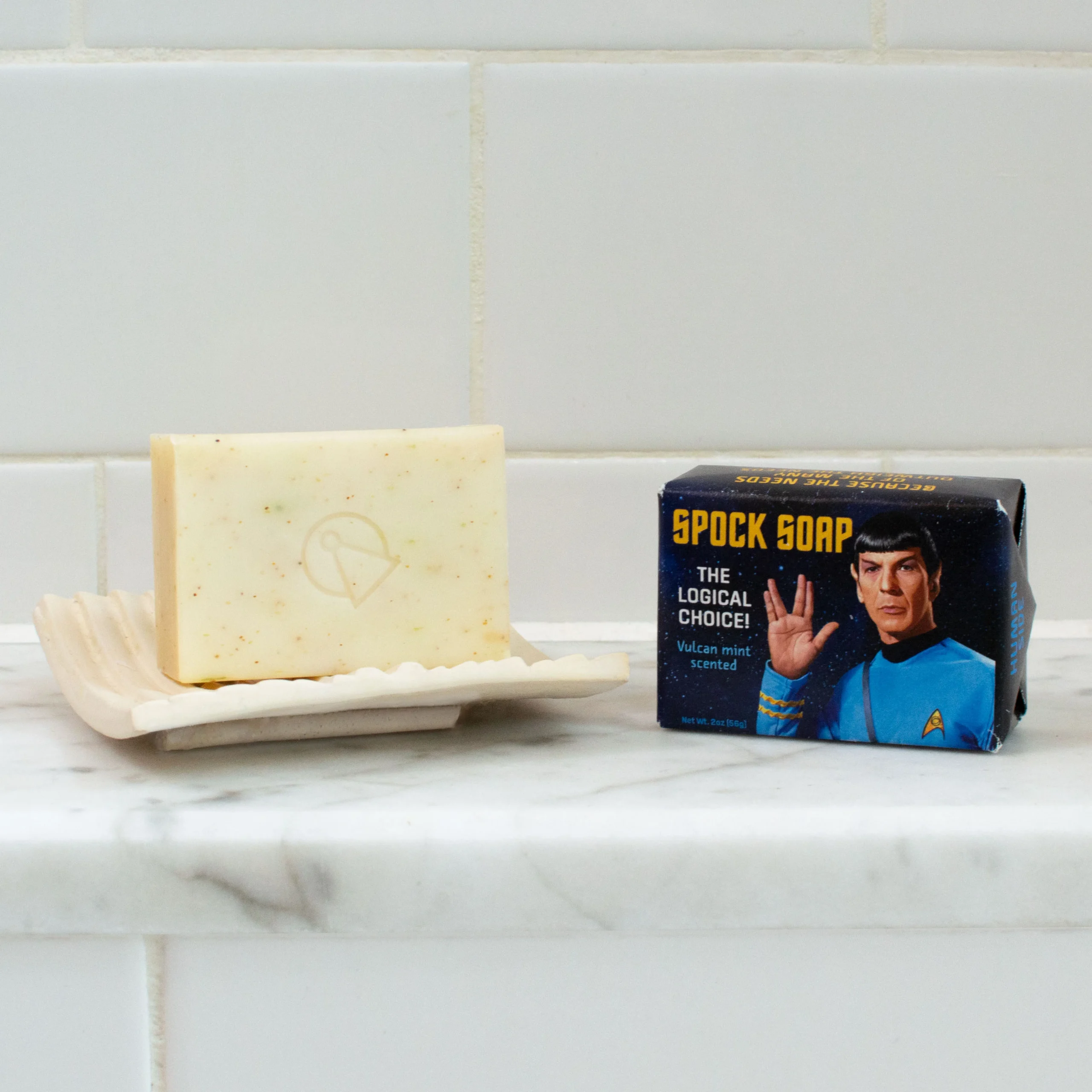 A bar of soap rests on a dish beside a box labelled Trump - Soap, featuring a character illustration. The curated items are placed on white marble with a tiled wall, creating an elegant concept store ambience. Gate21.ee