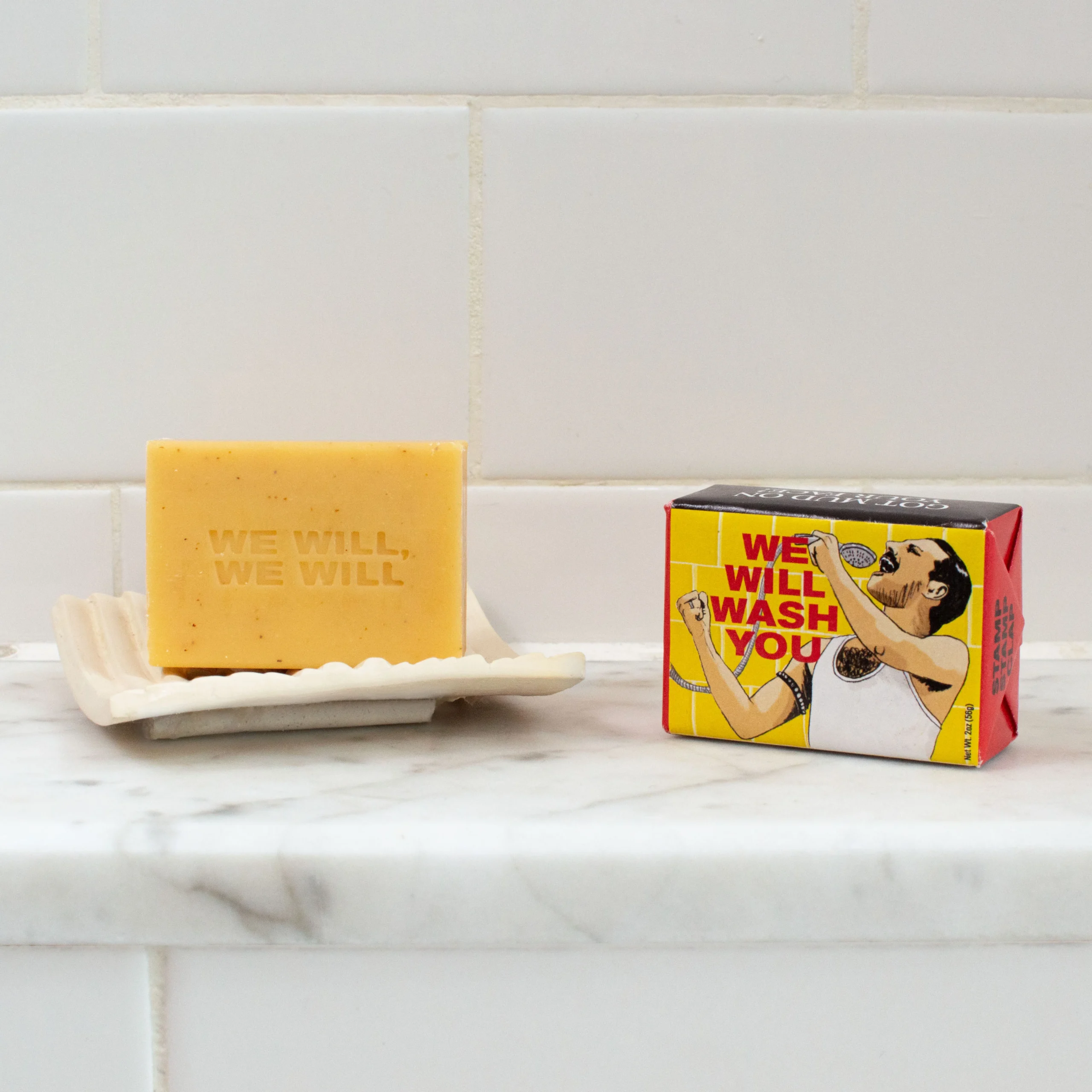 A bar of Trump - Soap engraved with WE WILL, WE WILL rests on a dish beside a box featuring an illustrated singer and bold WE WILL WASH YOU—an amusing and unique gift shop find for creative shoppers. Gate21.ee