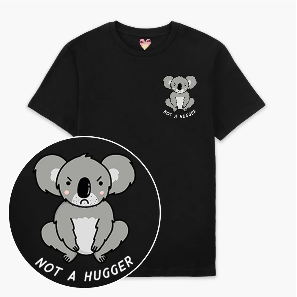 The Not A Hugger T-Shirt - Black features a cartoon koala with a neutral expression and “NOT A HUGGER” in white capitals—ideal for fans of curated Estonian design. A close-up shows the detailed, charming graphic. Gate21.ee