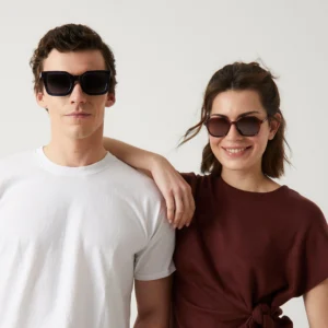 Two people pose against a plain background as if for a gift shop editorial. One wears a white T-shirt with "Cometa" Deep Blue Sunglasses; the other, in a maroon top, rests their arm on their companion's shoulder. Gate21.ee