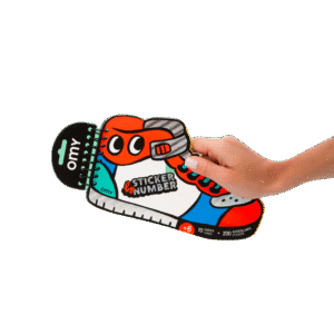 A hand holds &ldquo;Street - Sticker by Number & Postcards,&rdquo; a spiral-bound trainer-shaped sticker book with colourful cartoon art&mdash;perfect for finding unique, curated souvenirs during your Tallinn shopping adventures. Gate21.ee