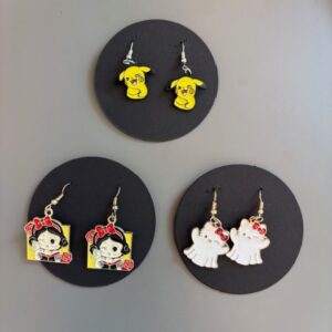 Three pairs of "Pins - korvar&otilde;ngad K&Otilde;IK" are displayed on black holders in this curated concept shop&mdash;perfect for Tallinn shopping: yellow Pikachu heads, cartoon skulls with bows and roses, and white ghosts with red bows. Gate21.ee