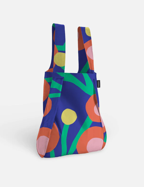 The Blossom – Special Edition reusable tote stands upright, showcasing bold orange, yellow, and pink circles with green curves on a dark blue background—a curated choice for gift shops and concept stores. Gate21.ee