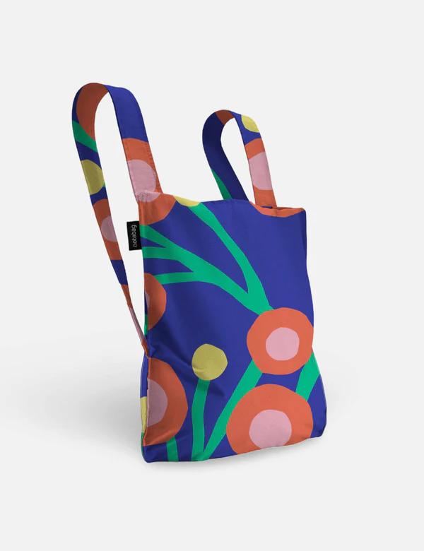 The Blossom - Special Edition is a reusable tote bag with a blue background and bold abstract floral patterns in orange, pink, green, and yellow—ideal for Tallinn shopping or carrying finds. It stands upright with visible handles against a white backdrop. Gate21.ee