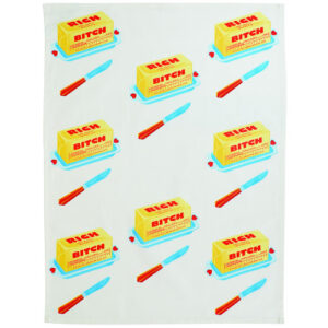 The “Rich bitch - Dish Towel” is a white cloth adorned with a tidy grid of yellow butter sticks labelled “RICH BITCH,” each accompanied by a blue and red butter knife and a blue butter dish, inspired by the playful style of BlueQ oven gloves. Gate21.ee