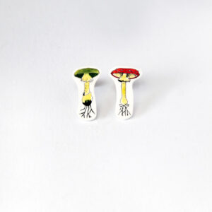 Värvilised Seened Kõrvarõngad: two whimsical mushroom-shaped earrings with faces—one green-capped, one red—both with visible roots, set against a white background. A charming choice for curated collections or Tallinn concept shops. Gate21.ee