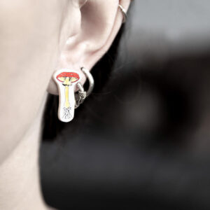 Close-up of an ear wearing three silver hoops and a vibrant Värvilised Seened Kõrvarõngad earring, curated for a concept shop celebrating unique Estonian design. Only part of the face and neck is visible against a blurred background. Gate21.ee