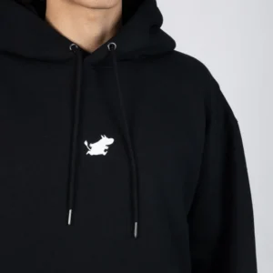 A person models the Moomin Hoodie - Black, which features a small white embroidered cartoon bull on the front. Only their lower face, neck, and upper torso are visible. Gate21.ee