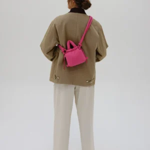 A person stands facing away from the camera, wearing neutral-toned clothing and carrying the Micro Ona Soft Bag - Pink—an eye-catching accessory for exploring new ideas at a concept store. The background is plain white. Gate21.ee
