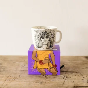 The Long-legged Legend - Big cup is a white mug with a smiling woman's head and hands, paired with a purple box showing her body in an orange fringed dress—a striking gift shop pick for Tallinn shopping fans. Gate21.ee