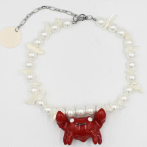 The CACKO - Necklaces - K&Otilde;IK features round and irregular white beads, a smiling red crab-shaped pendant, metal chain extender, and a white tag&mdash;an ideal pick for fans of playful Estonian design. Gate21.ee