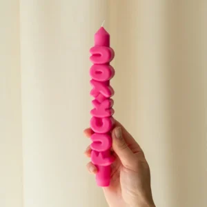 A hand displays the F*ck You 3D Candle - Pink, featuring raised letters with a bold phrase, perfect as a standout piece for gift shops or concept stores. The bright pink candle contrasts against a soft, neutral background. Gate21.ee